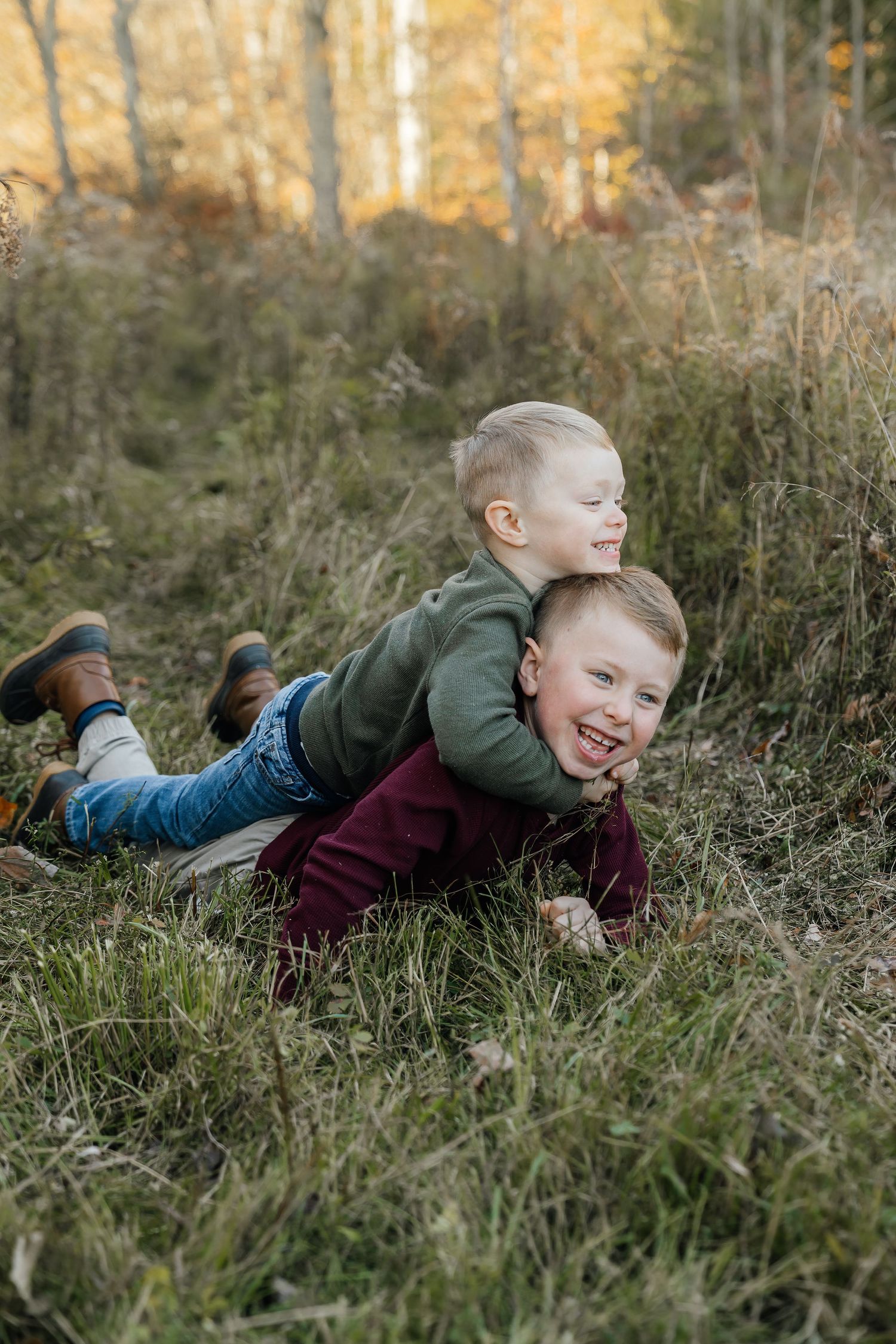 Two children playing and laughing while laying in tall grass.