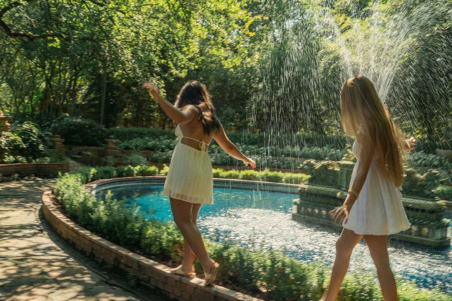 Friends playing and dancing near a tranquil garden pond on a sunny summer day.