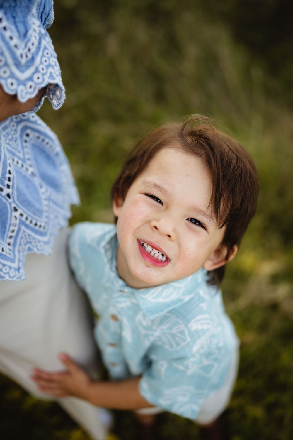 A joyful child in blue clothing smiles brightly in an outdoor portrait.
