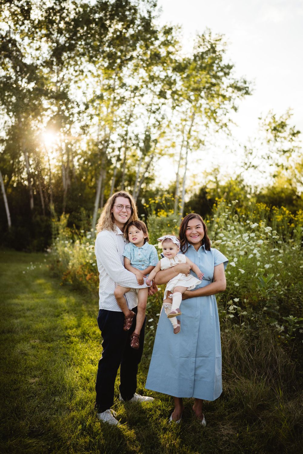 Family poses together in wildflower meadow during sunset photoshoot.