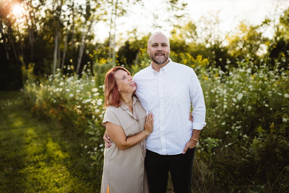 Couple embraces while standing in wildflower field at golden hour.