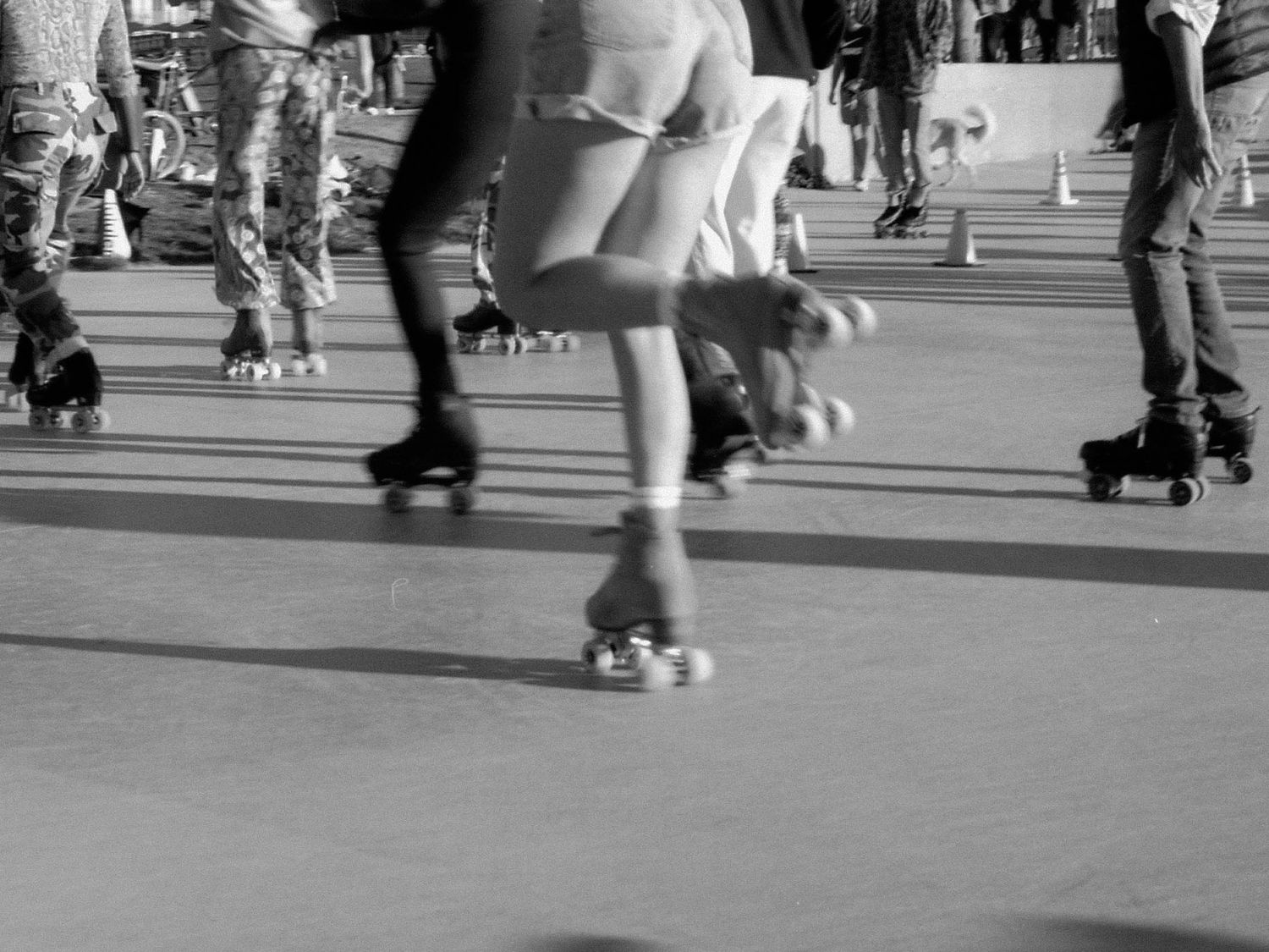 Black and white image of people roller skating in Venice Beach on a smooth surface.