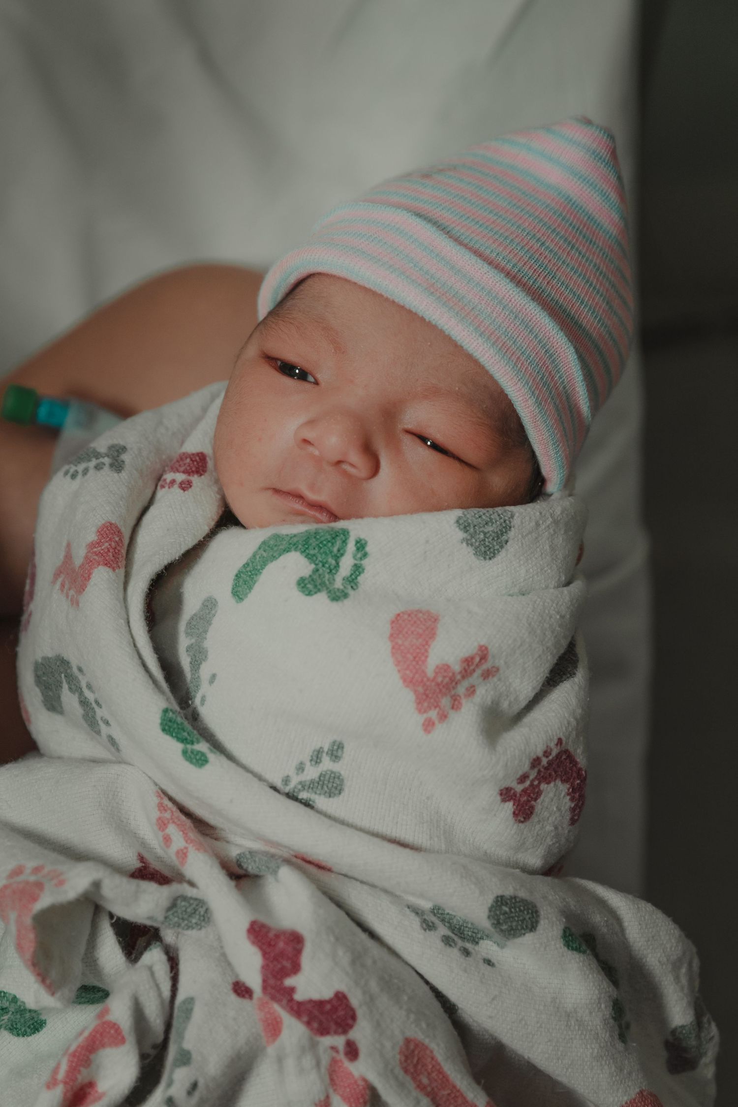 Newborn baby wrapped in patterned blanket wearing striped hat while resting.