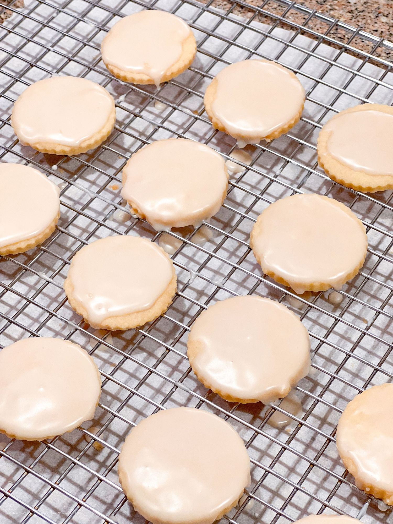 Freshly baked sugar cookies with pale pink icing arranged on a cooling rack.