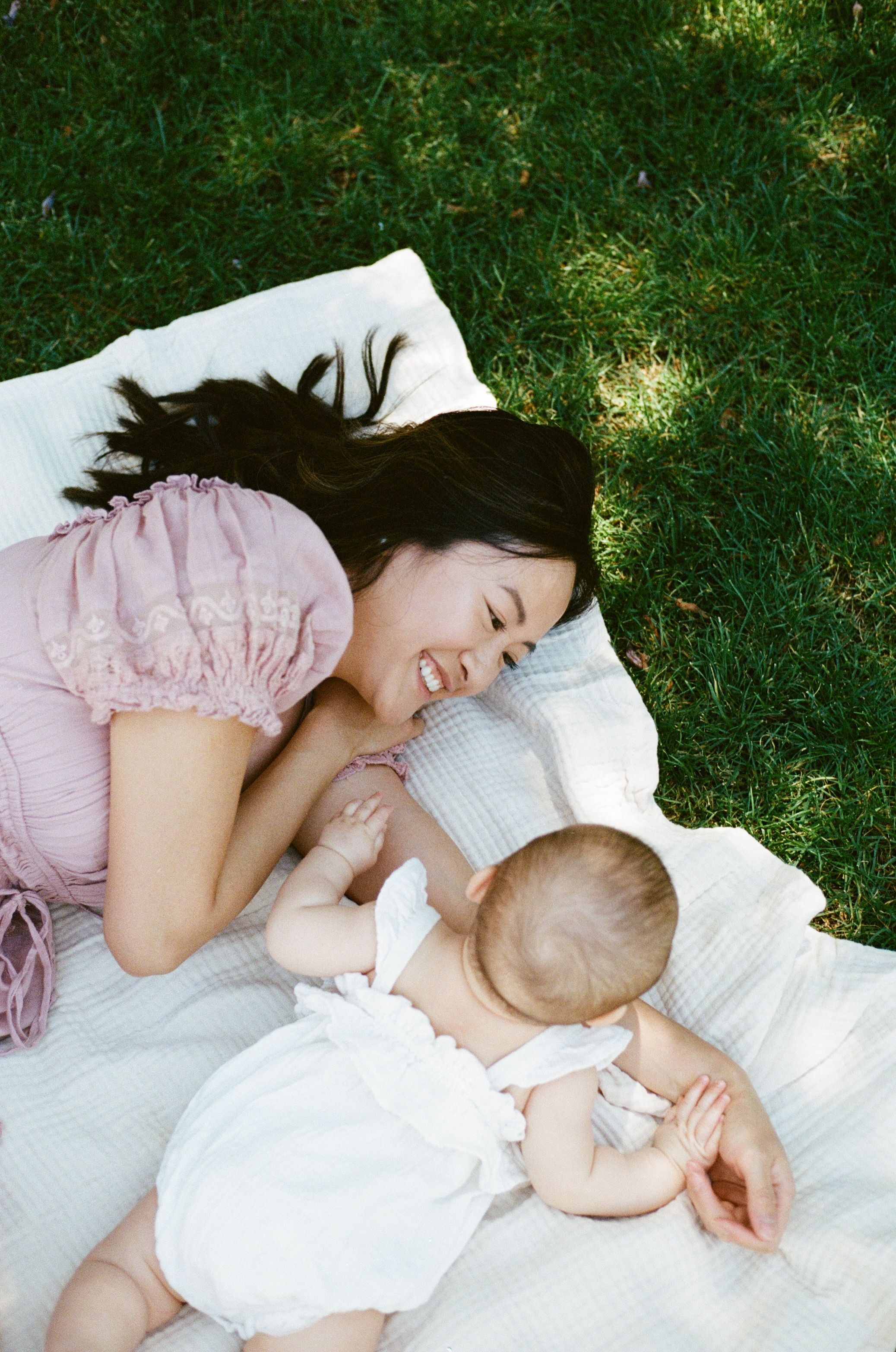 A tender moment captured on a white blanket in the grass with mother and baby.