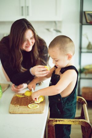 Person in green apron leans over wooden cutting board to smell fresh citrus fruit in rustic kitchen setting.