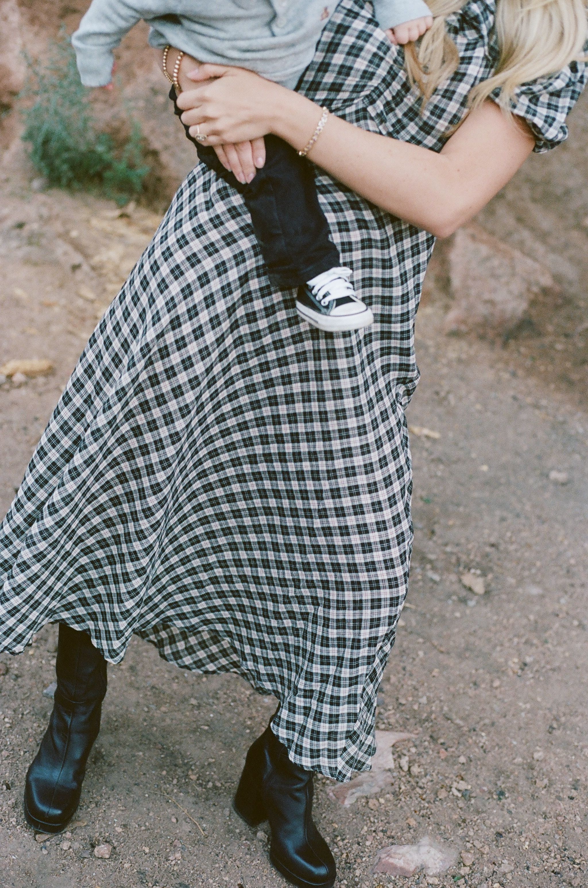 Person wearing plaid dress and boots holds tiny baby shoe.