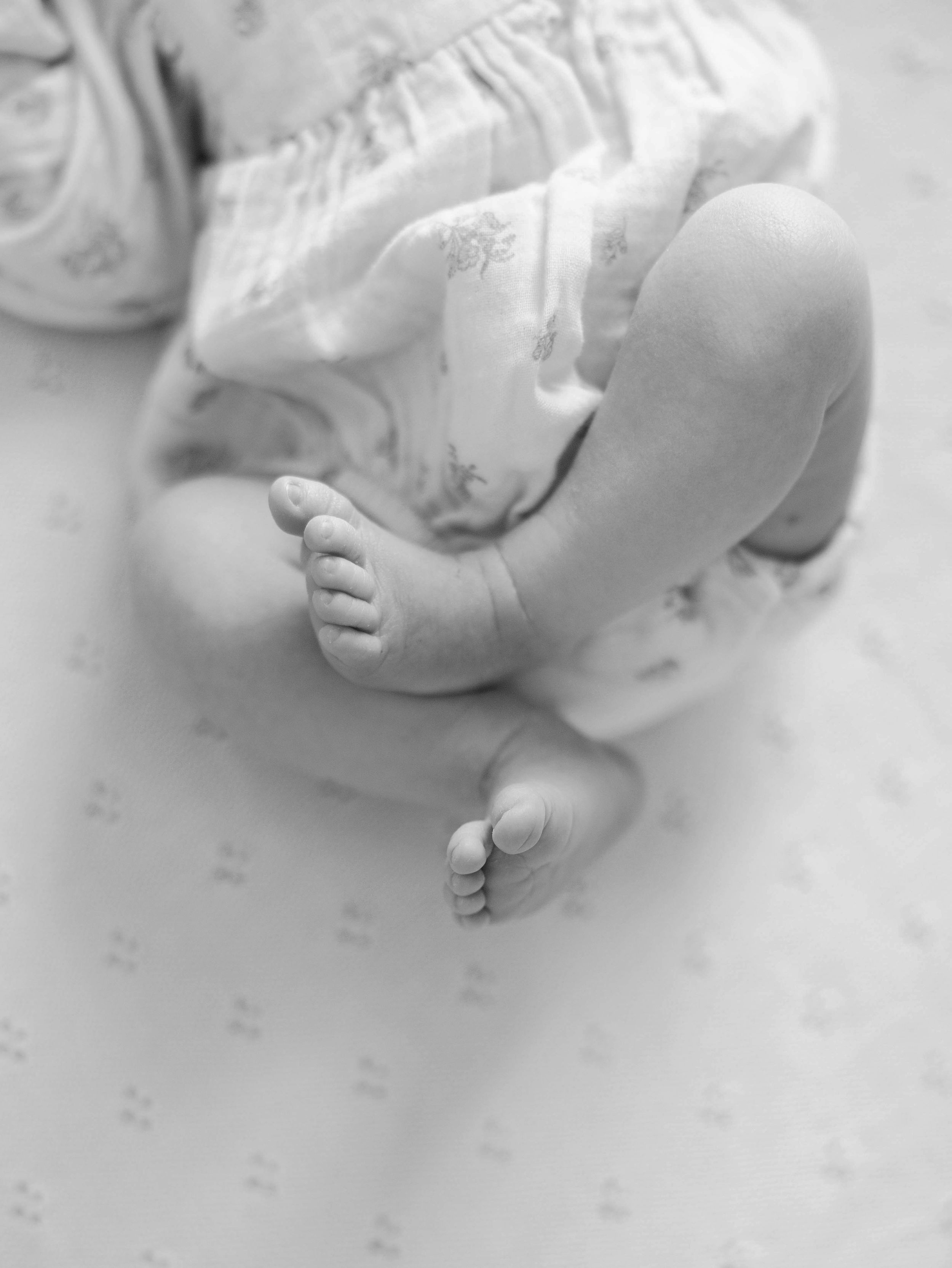 Close-up black and white photo of baby feet against white bedding.