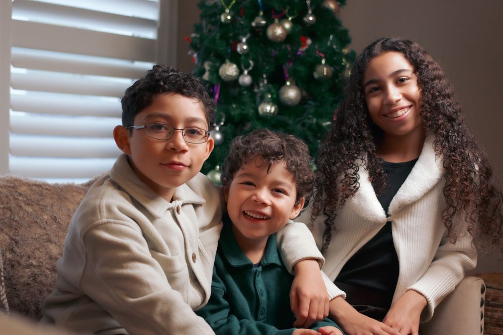 Family of three sitting on a couch with a decorated Christmas tree in the background.