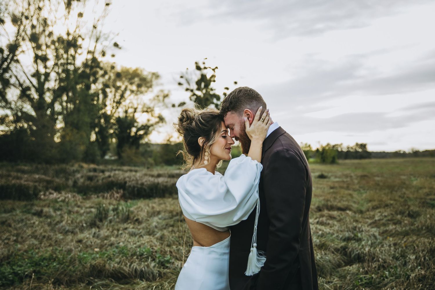 Intimate outdoor portrait of newlyweds embracing in a natural field at sunset.