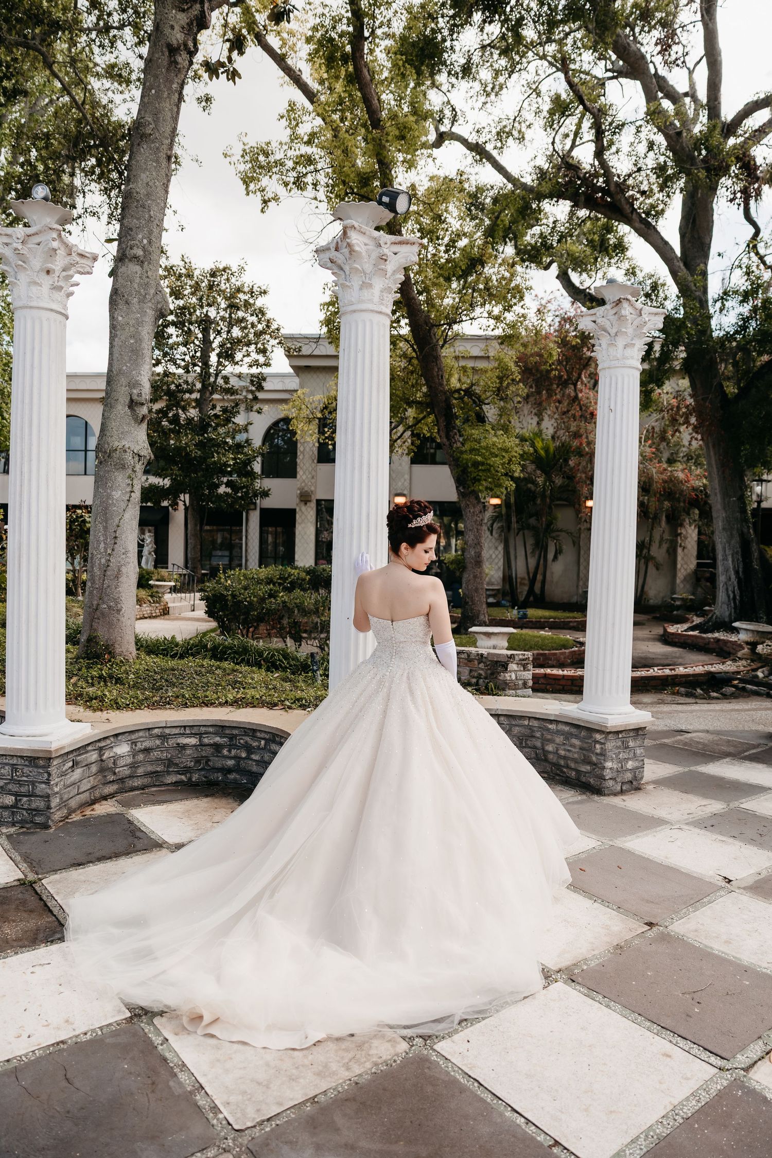 Wedding dress with flowing train photographed in garden setting with white columns.