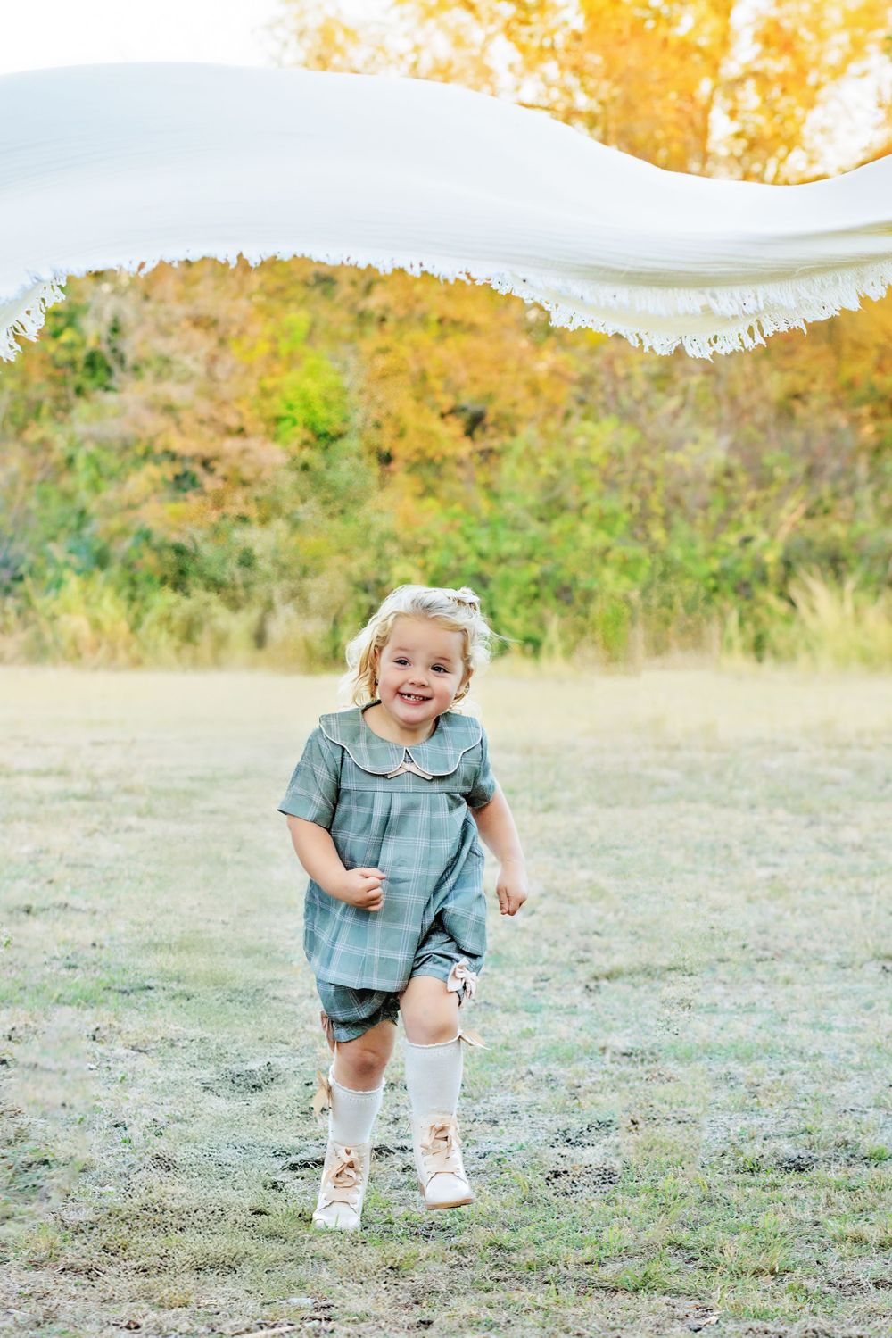 Playful child running and laughing in a grassy field during golden hour wearing a blue dress and white knee socks.