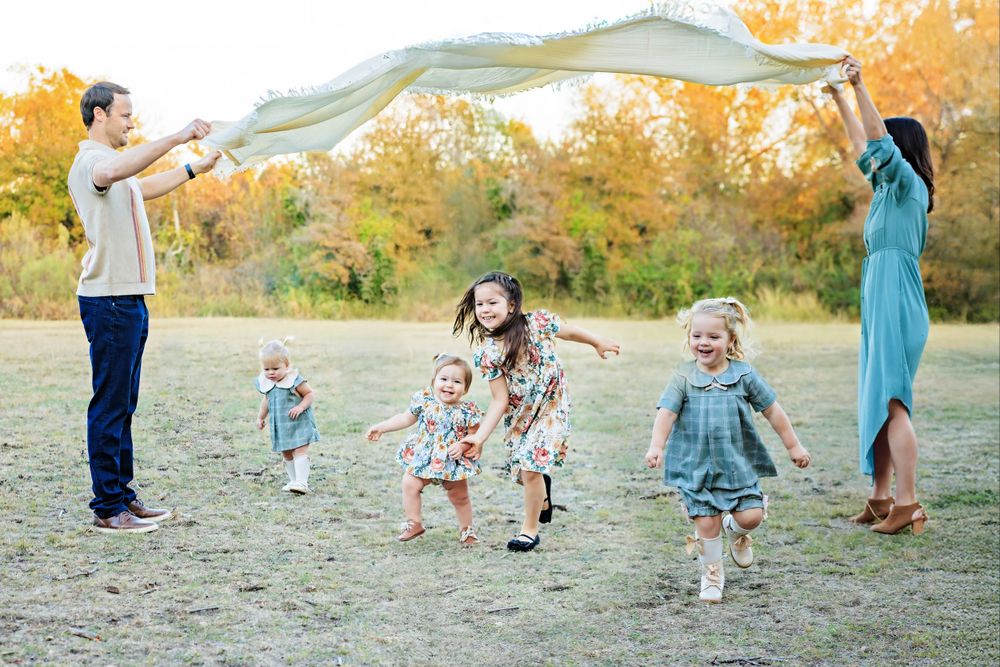Group playing together under blanket in autumn field with golden trees in background.