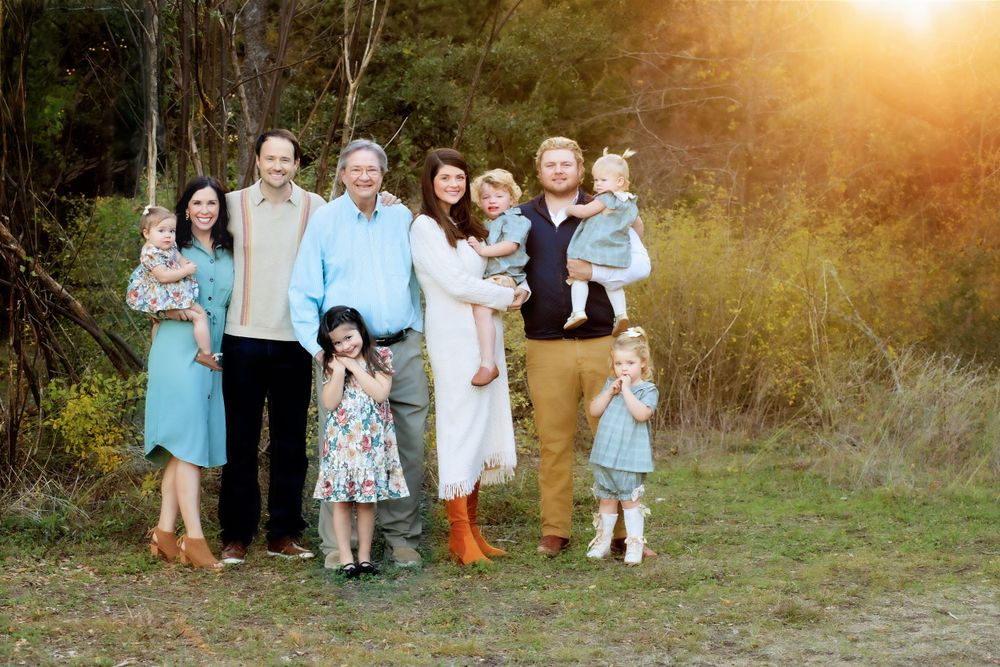 A family group poses together outdoors at sunset with warm golden lighting in a natural wooded setting.