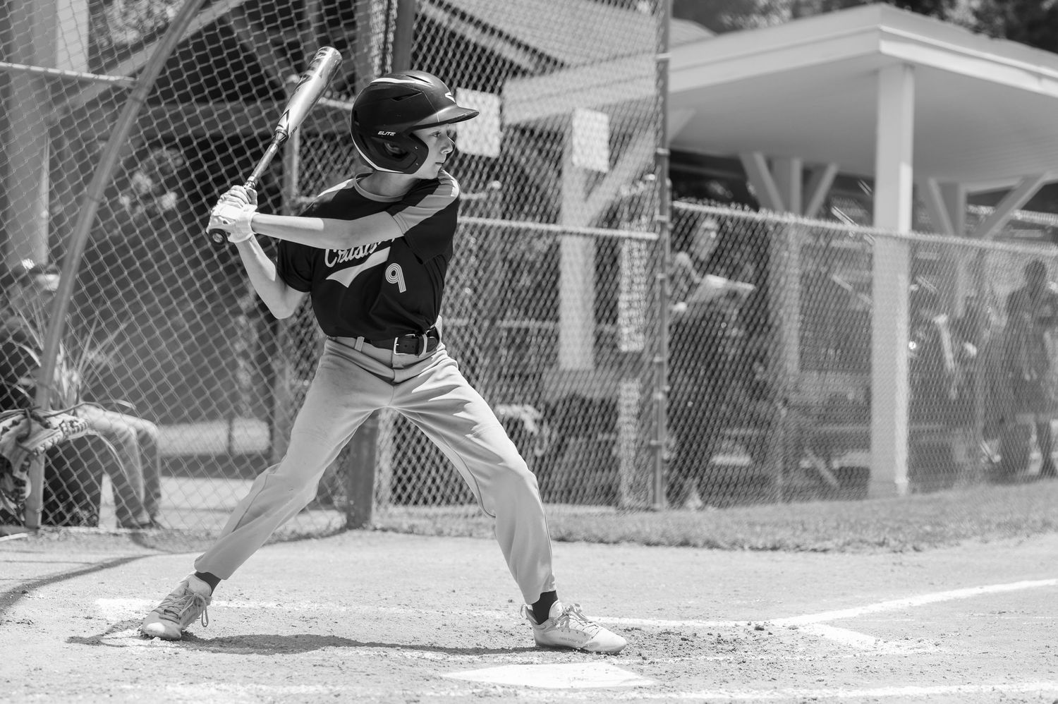 Baseball batter in black uniform takes stance at home plate during game.