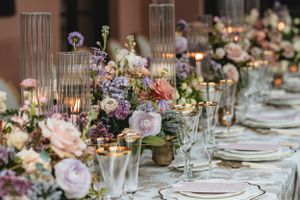 An elegant wedding table setting features pink and purple floral centerpieces with glowing candlelight and crystal glassware.