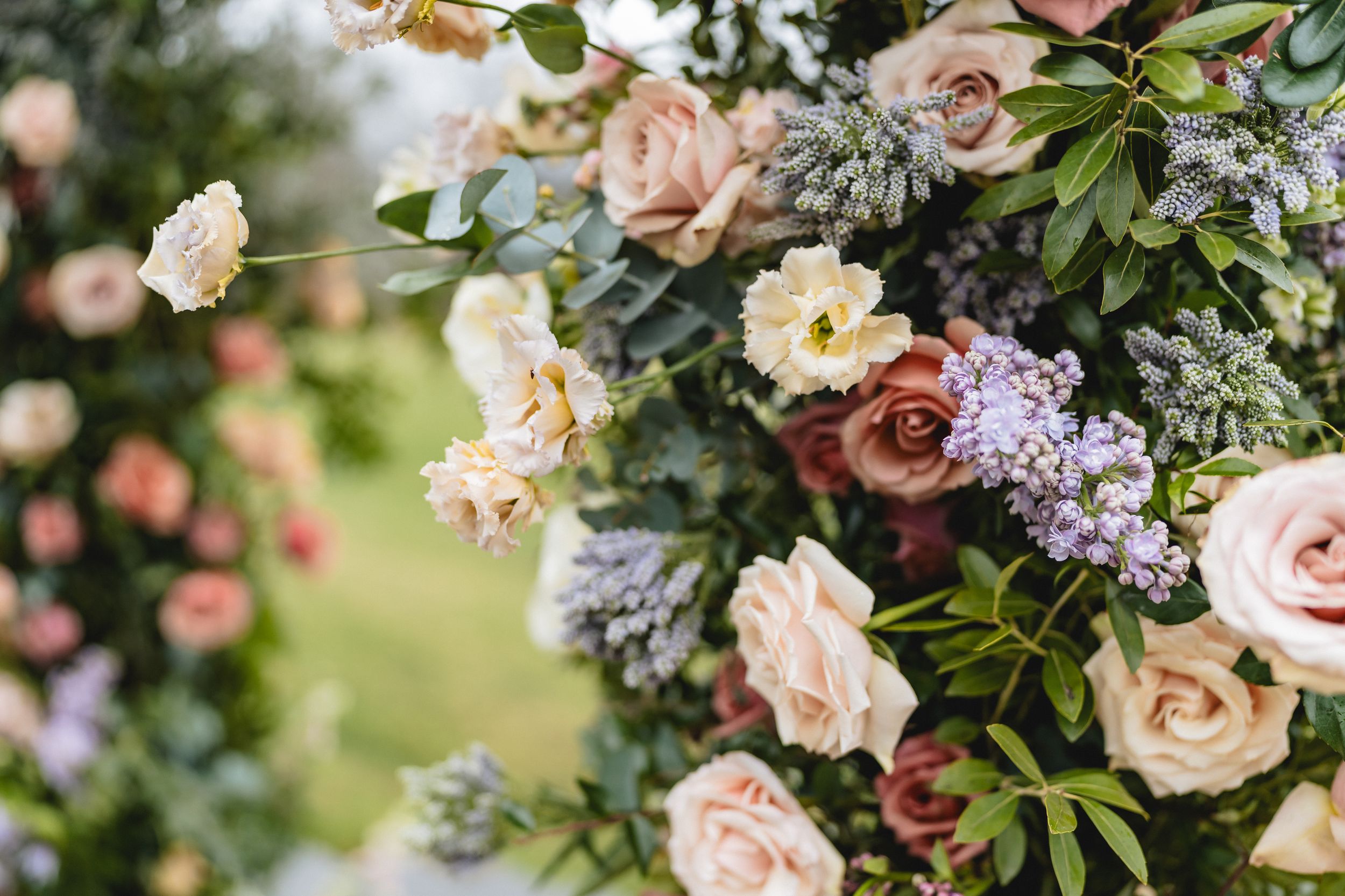 Soft pink roses and lilac flowers arranged in a romantic garden-inspired floral display with lush greenery.