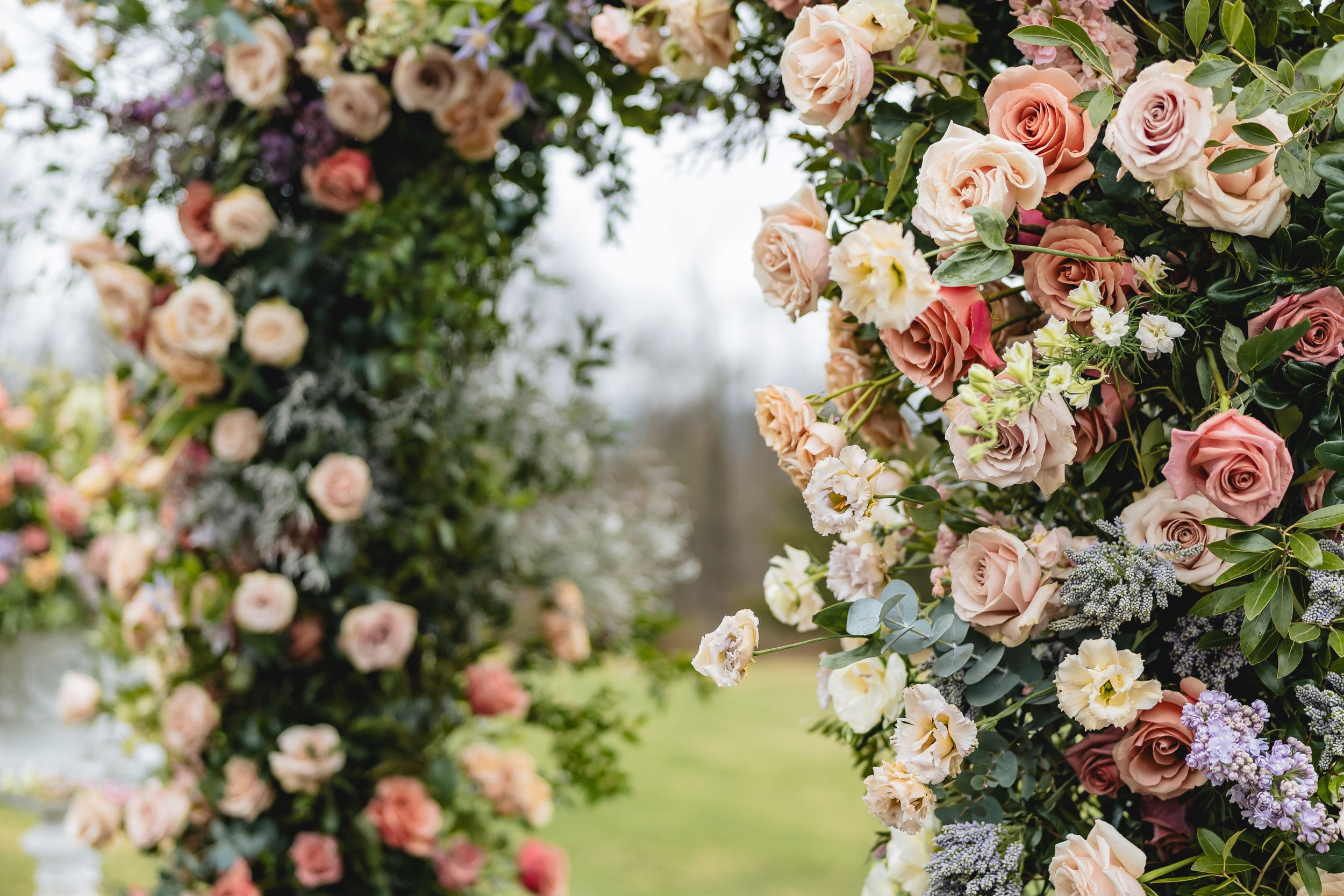 Beautiful floral arch with pink and cream roses and delicate greenery framing an outdoor garden view.