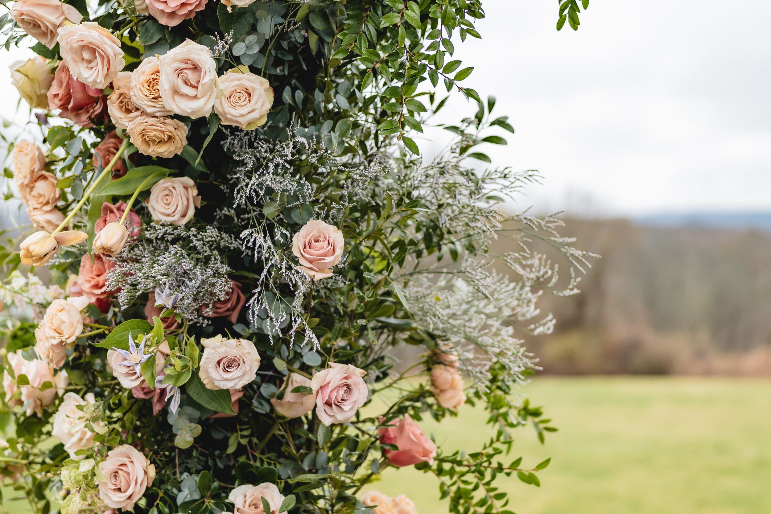 Beautiful peach roses and greenery adorn an outdoor wedding arch with a scenic mountain landscape in the background.