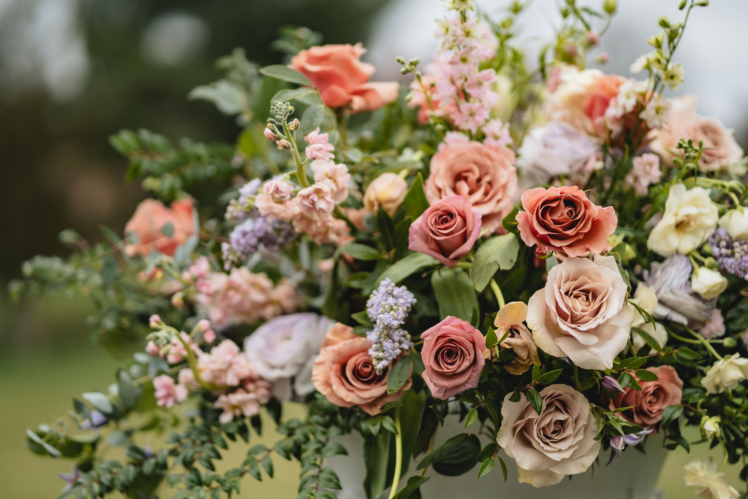 Close-up of romantic pink and peach rose wedding bouquet with mixed flowers and greenery.