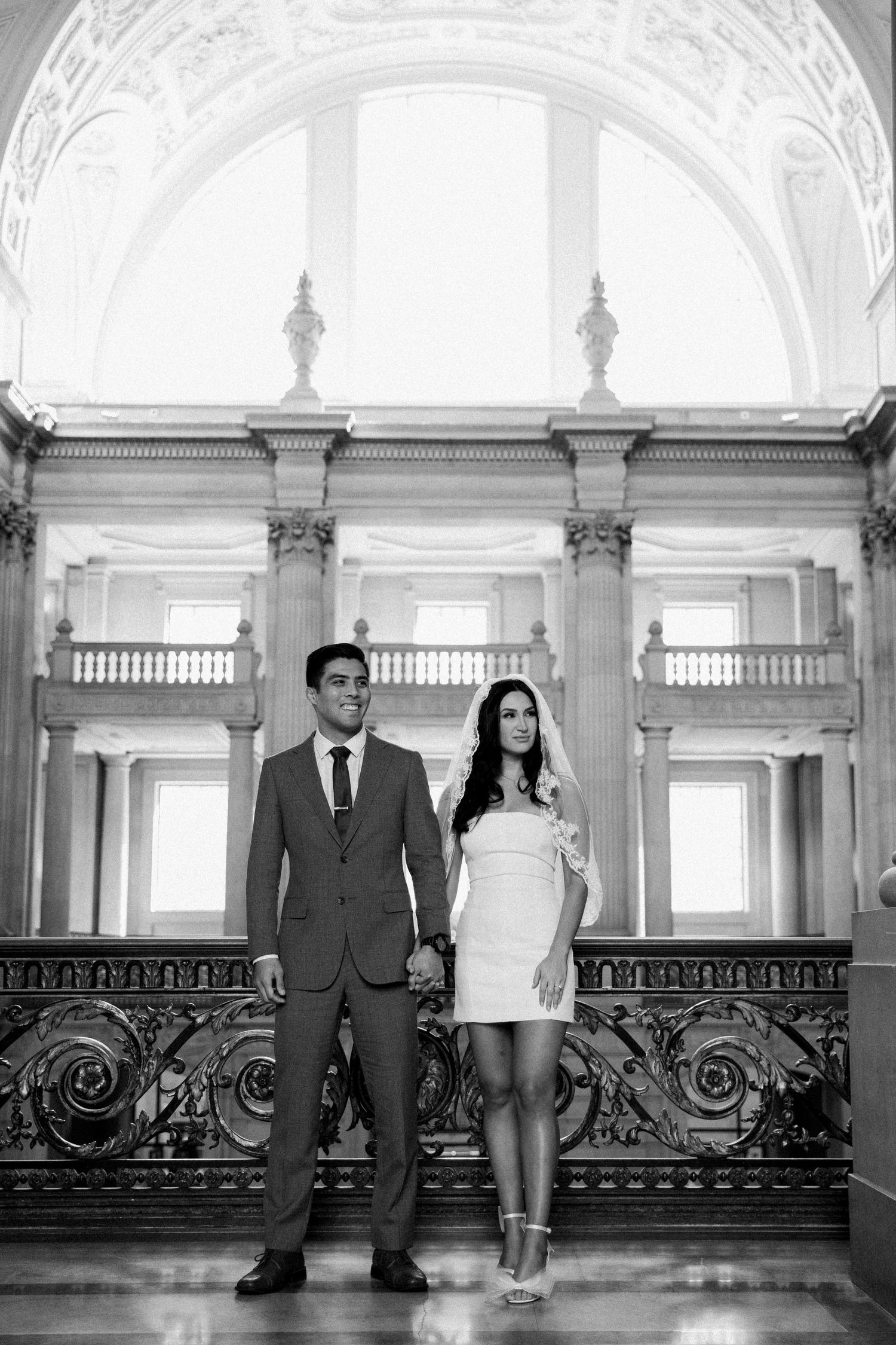 Eloping Bride and Groom holding hands in front of the beautiful, white marble atrium of San Francisco City Hall just above the Grand Stairs