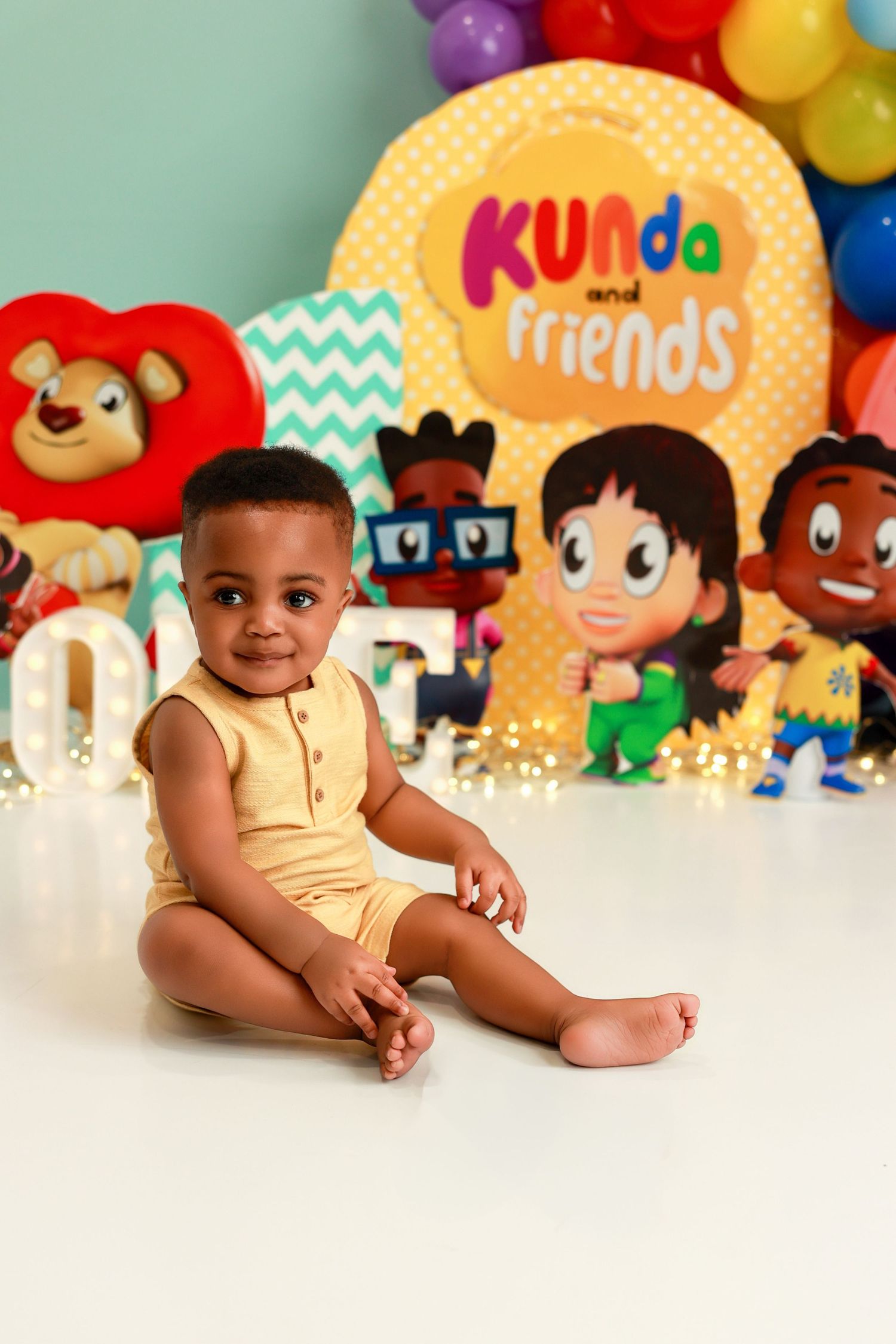 Colorful birthday party setup with balloons, decorations and toys against a white background.