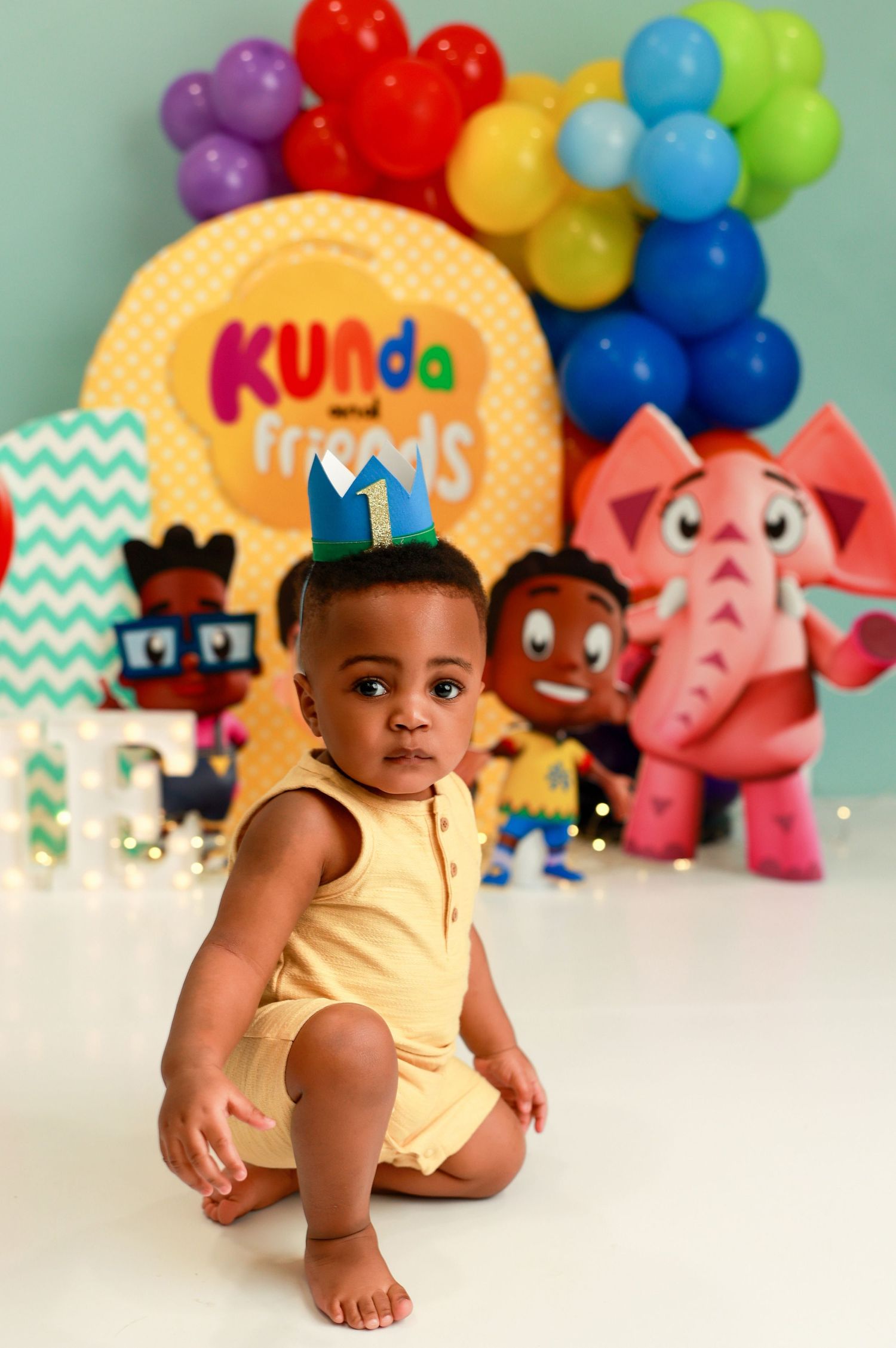 Colorful balloon arch and playful stuffed animals create a cheerful backdrop for a baby photo session.