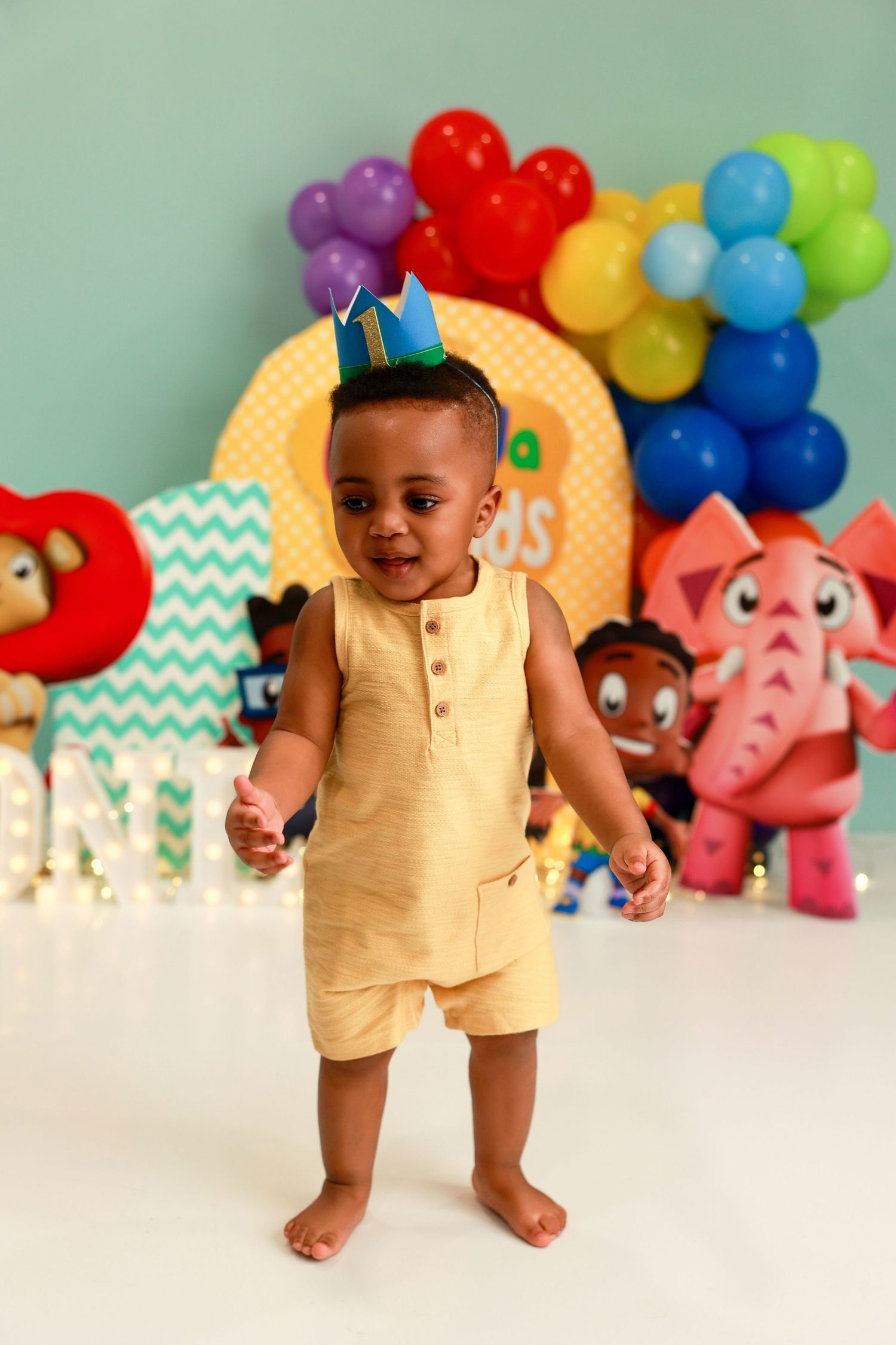 Festive birthday celebration with colorful balloons and cartoon decorations as baby explores party setup.