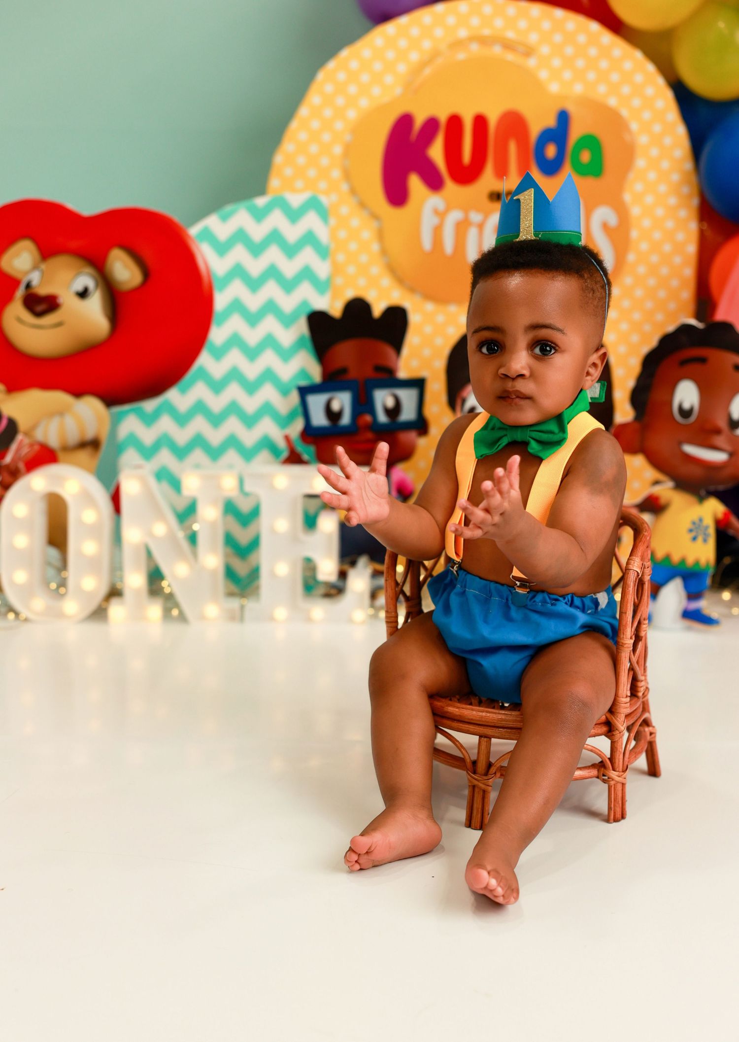 Colorful first birthday party setup with decorative letters spelling ONE, stuffed animals, and a festive Kunda backdrop.