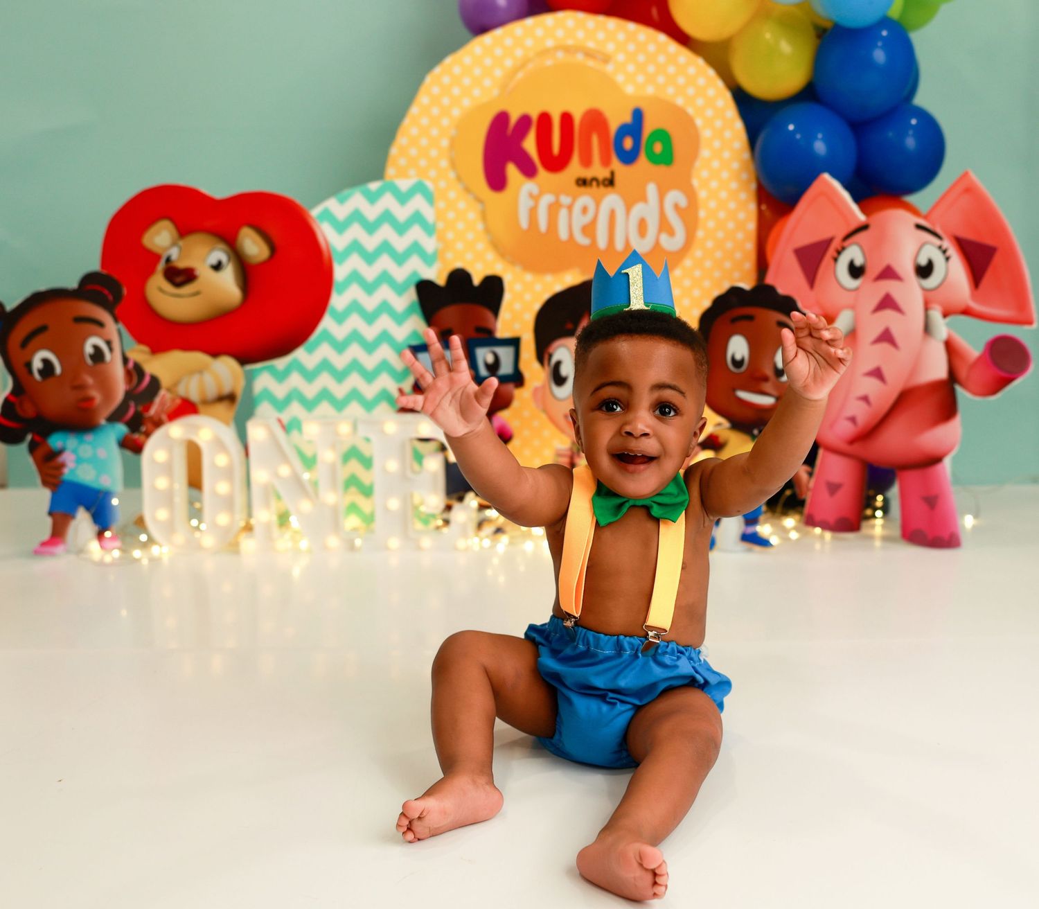 A colorful collection of KUNda toys and plush characters displayed on a white surface with decorative party elements.