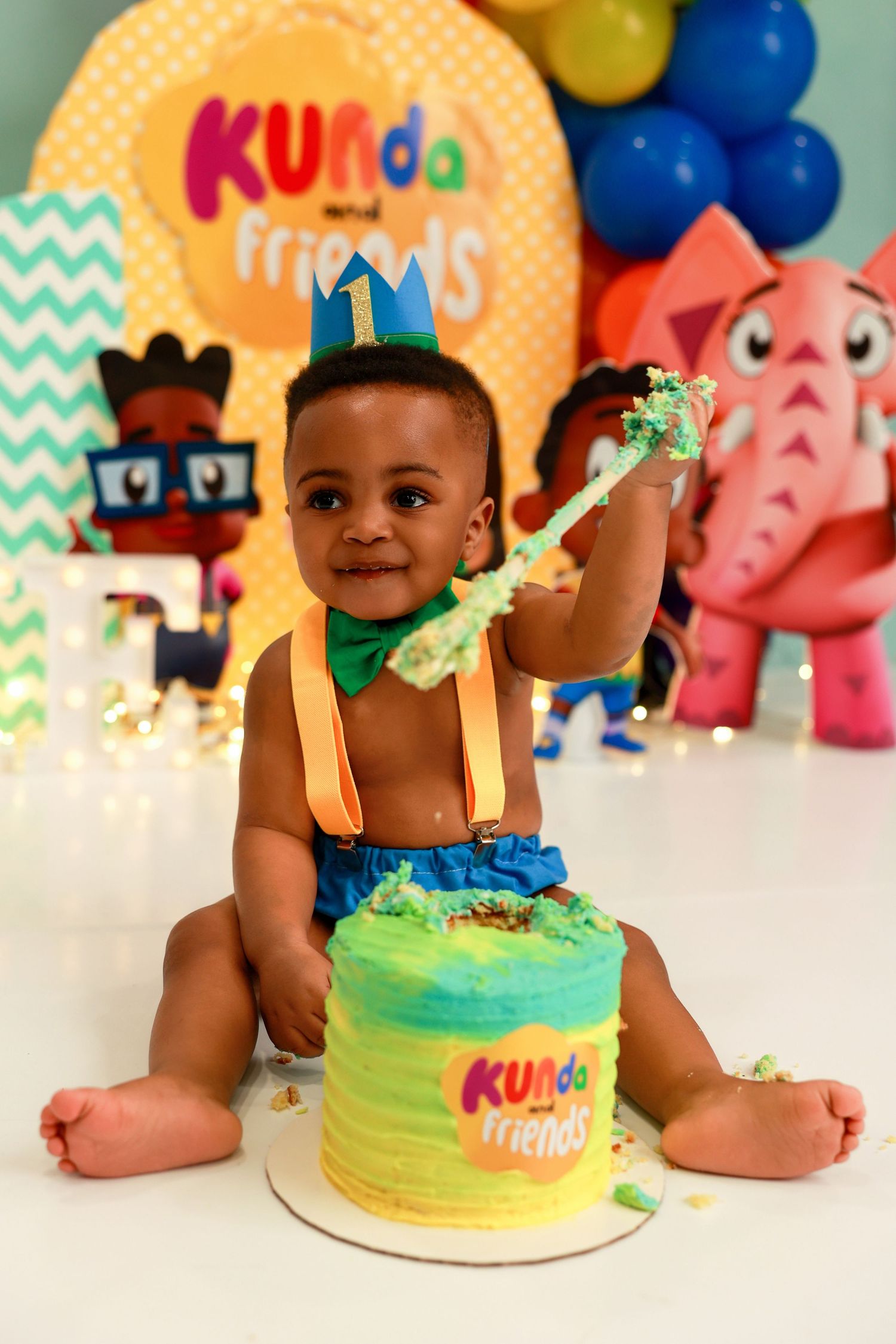 Colorful first birthday party setup with cake, balloons, and decorative elements in teal and orange tones.