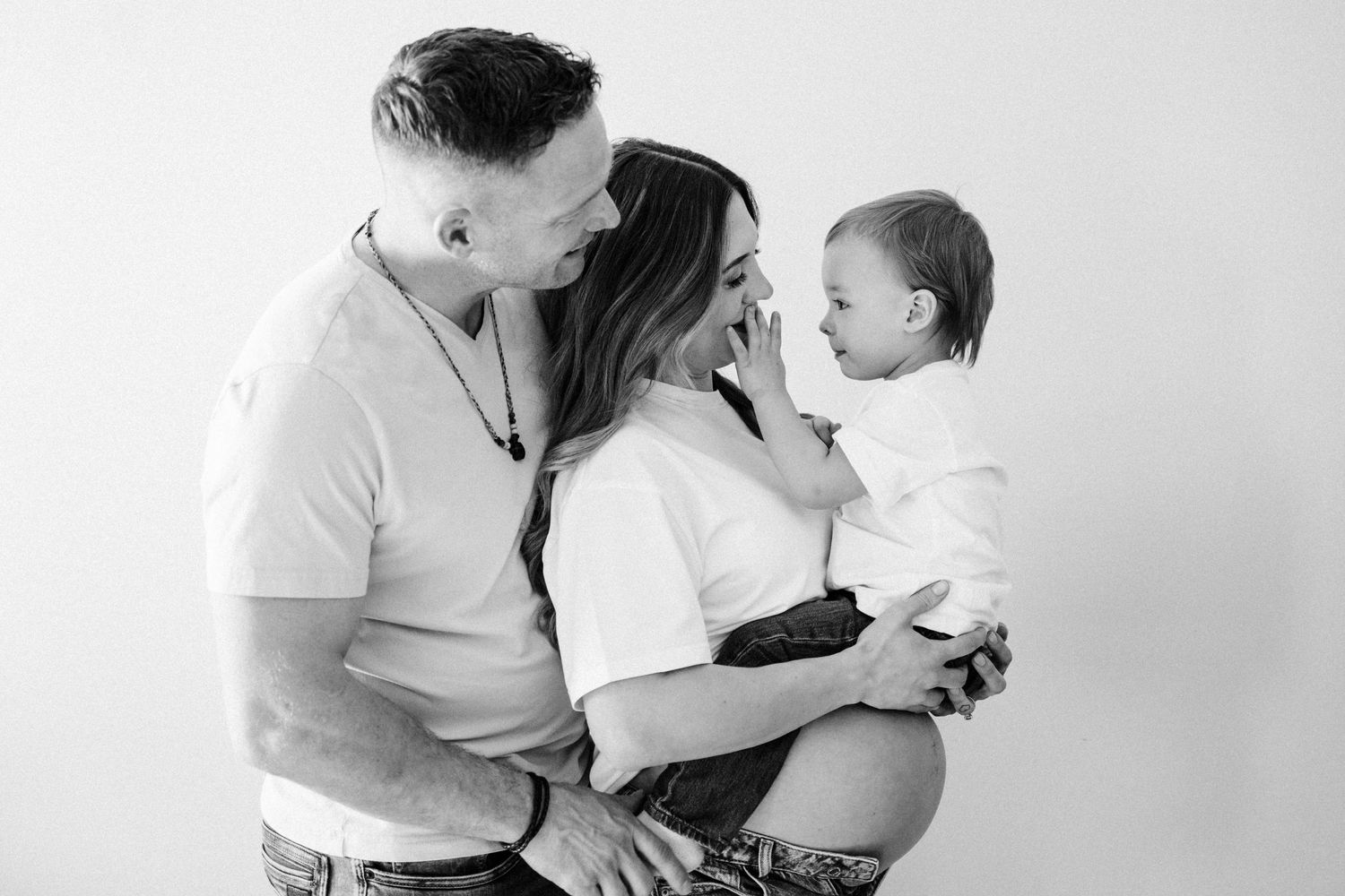 A black and white portrait of a family embracing and smiling together against a white background. Fort McMurray Photographer