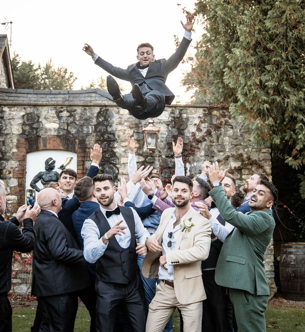 Groomsmen in suits jumping and celebrating outdoors with enthusiasm.