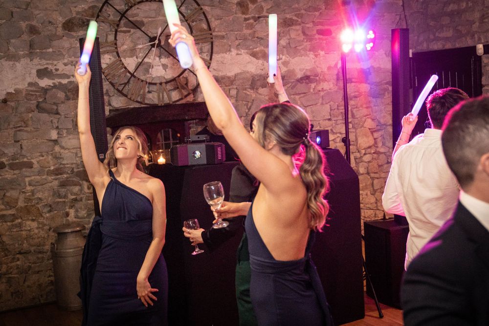 Wedding guests dancing and celebrating in rustic stone venue with pink lighting.