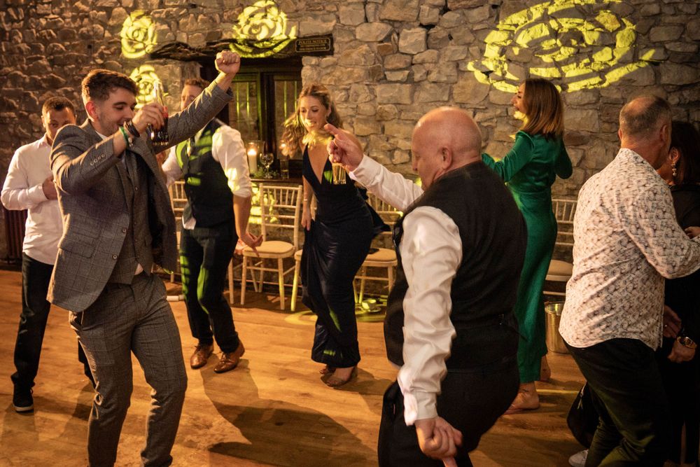 Wedding dance party with guests celebrating on dance floor in rustic stone venue.