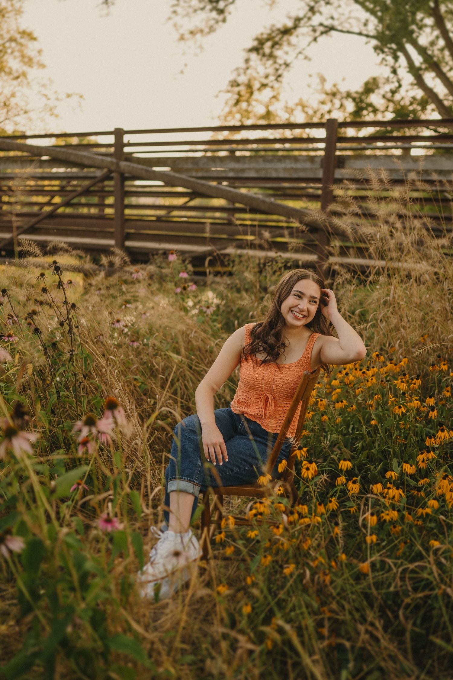 A golden sunset illuminates a wildflower field with orange blooms and a wooden fence in the background.