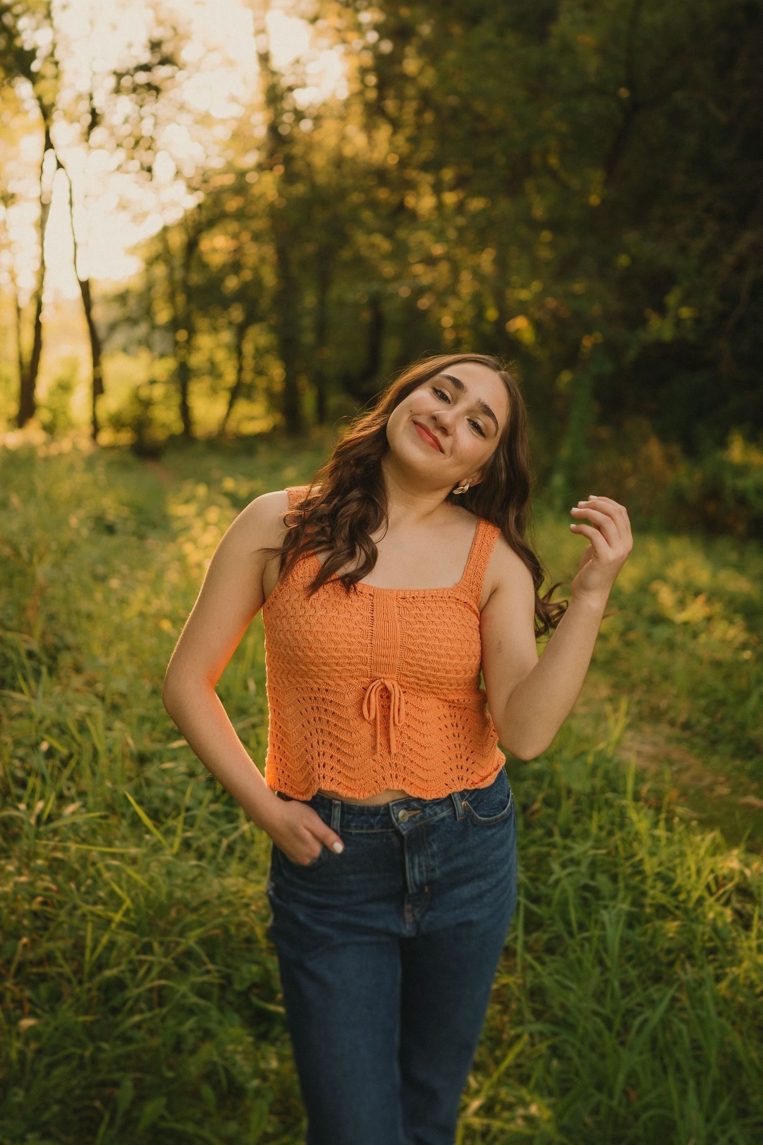 An orange knit top and jeans outfit captured in warm evening sunlight against lush greenery.