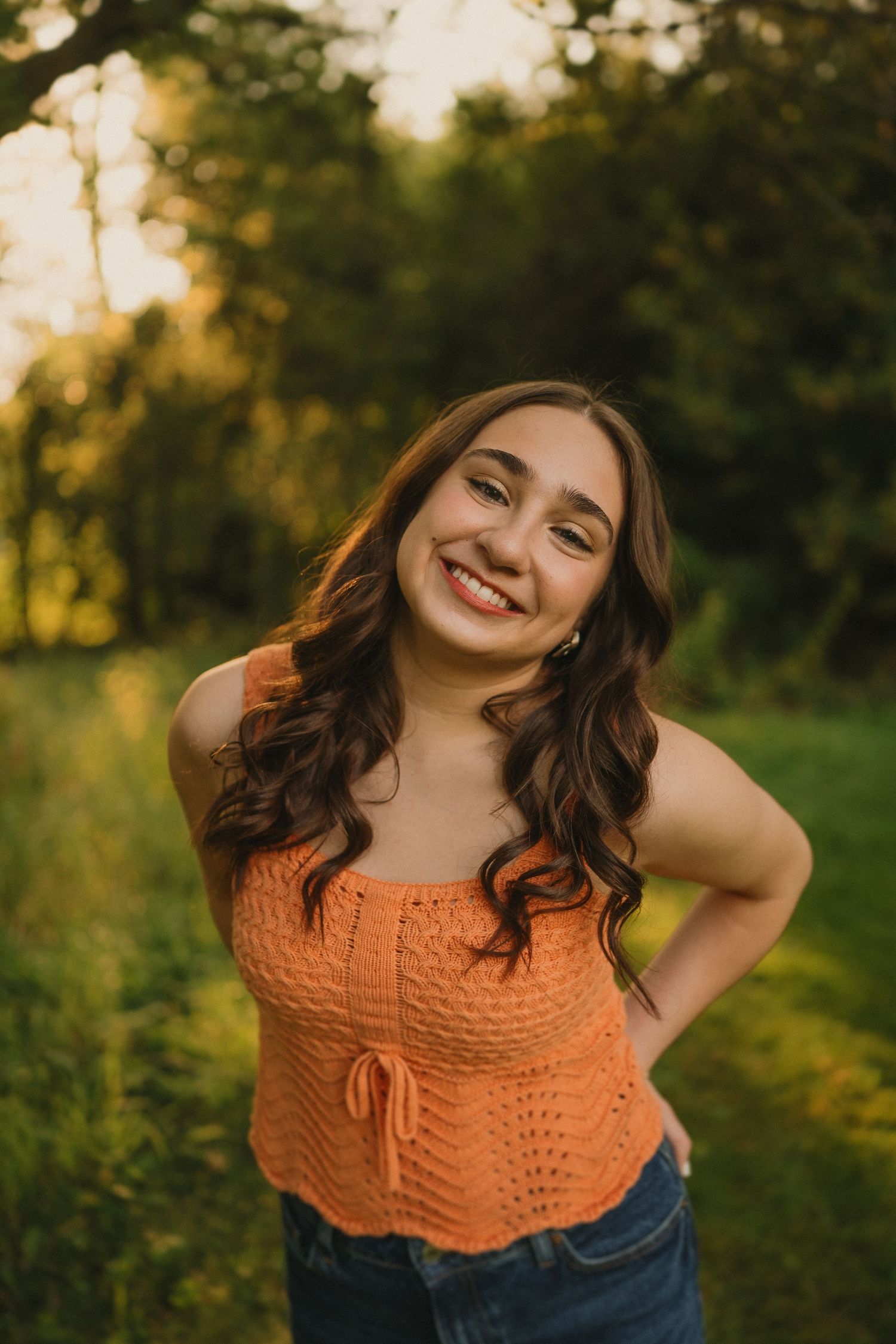 Casual summer portrait featuring an orange crochet top against a sunlit natural backdrop.
