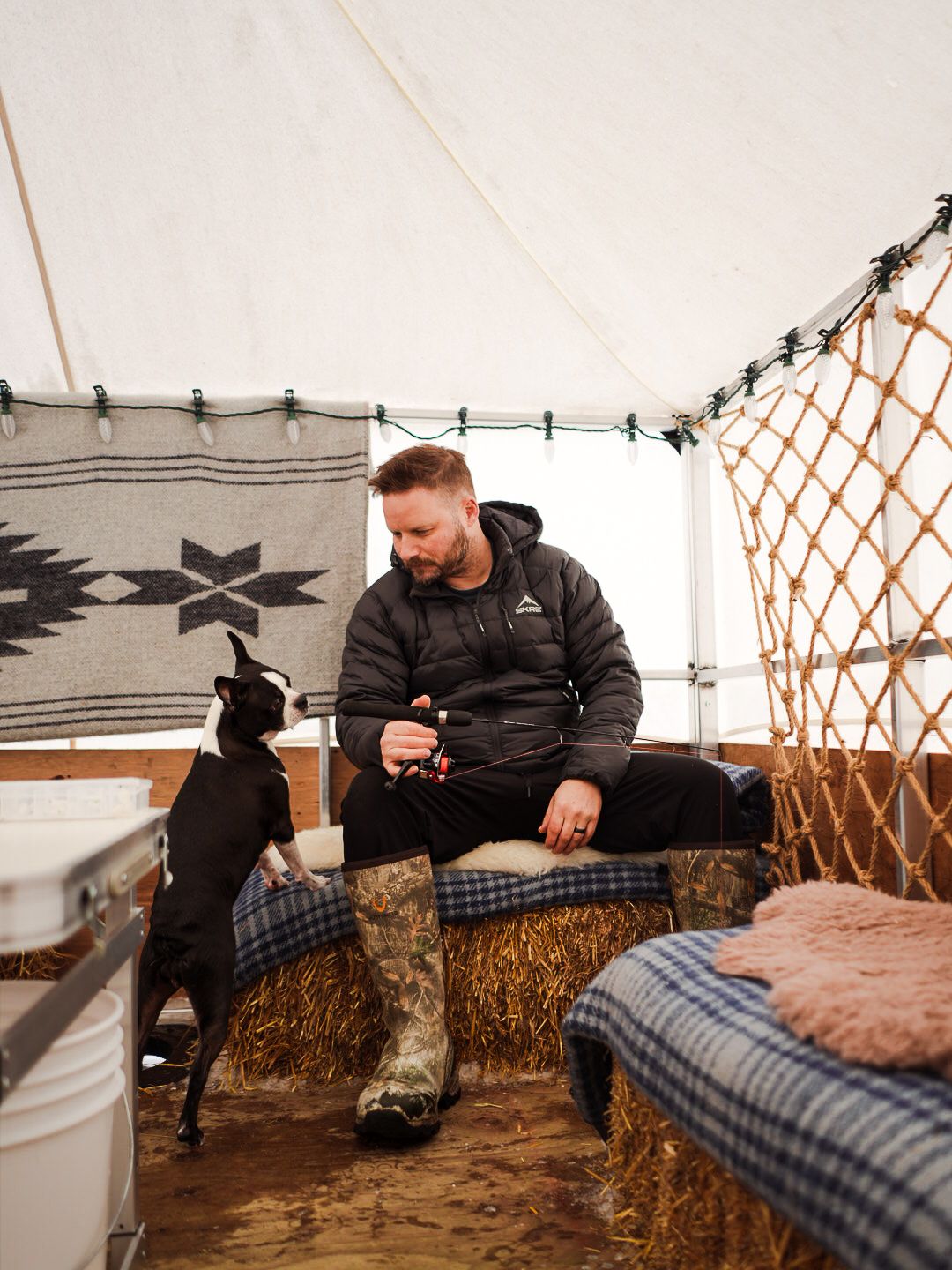 Rustic tent interior with plaid blankets and hay bale seating.