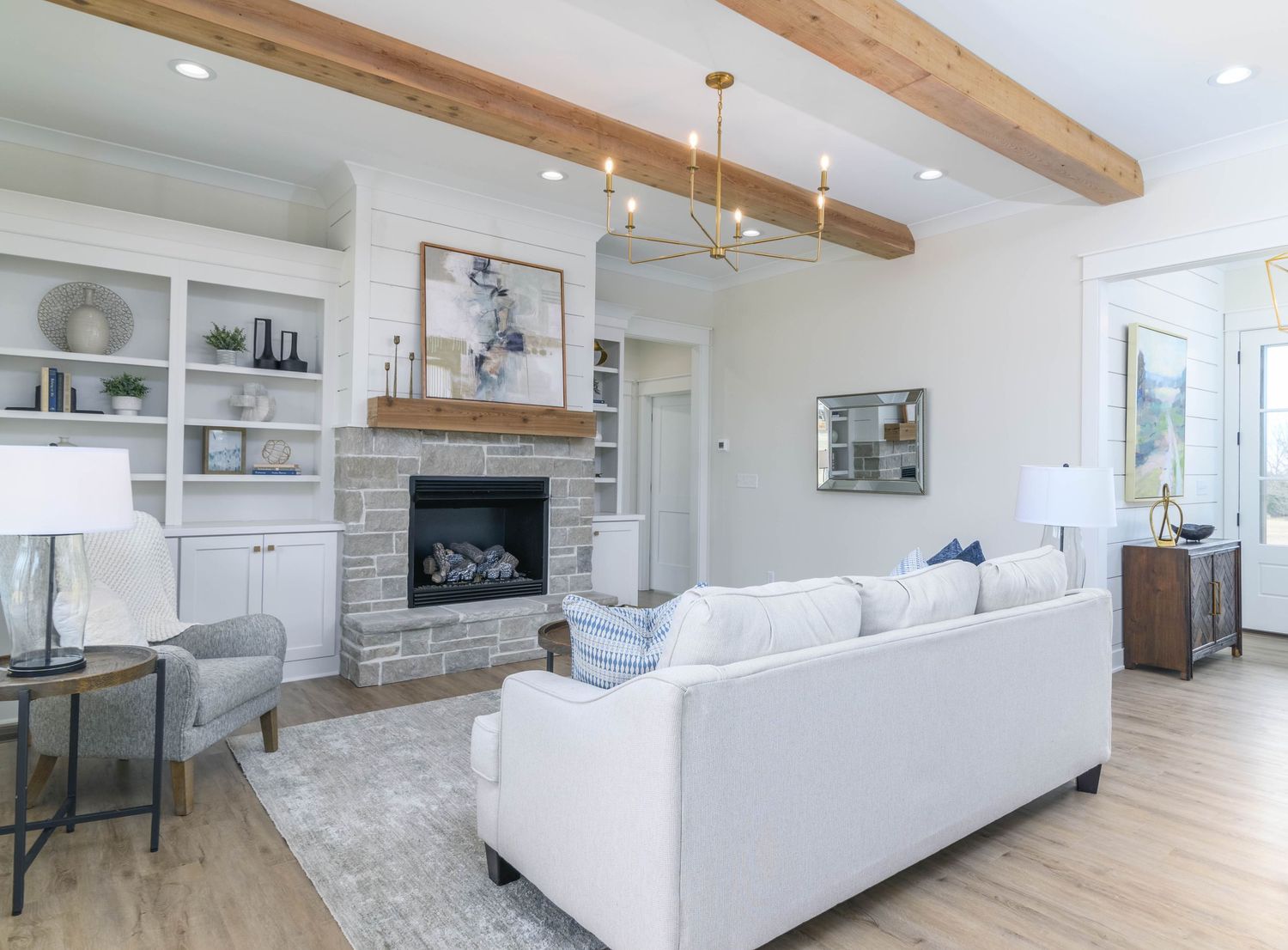 Modern living room with white sectional sofa, stone fireplace, exposed wood beams, and built-in shelving.