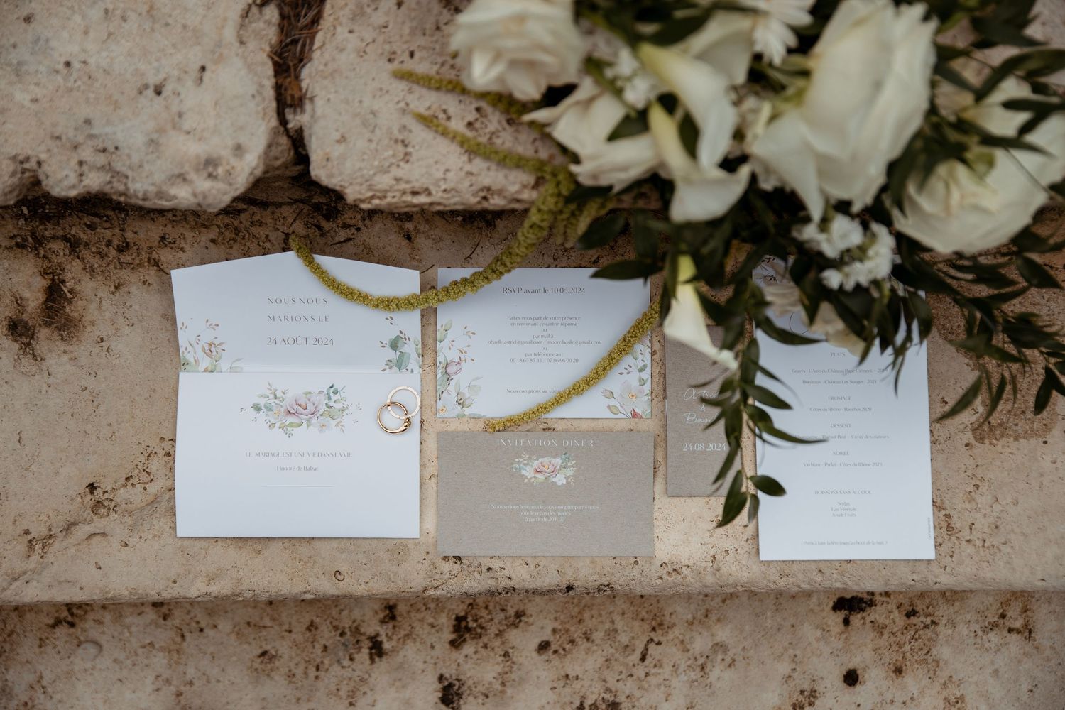 Elegant white wedding invitations displayed with roses against textured stone.