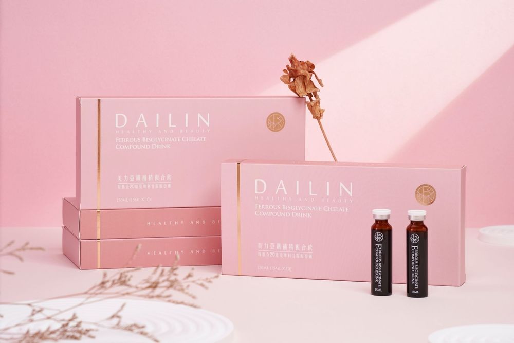 Pink Dailin tea boxes with black bottles displayed on pink background with dried flower accents.