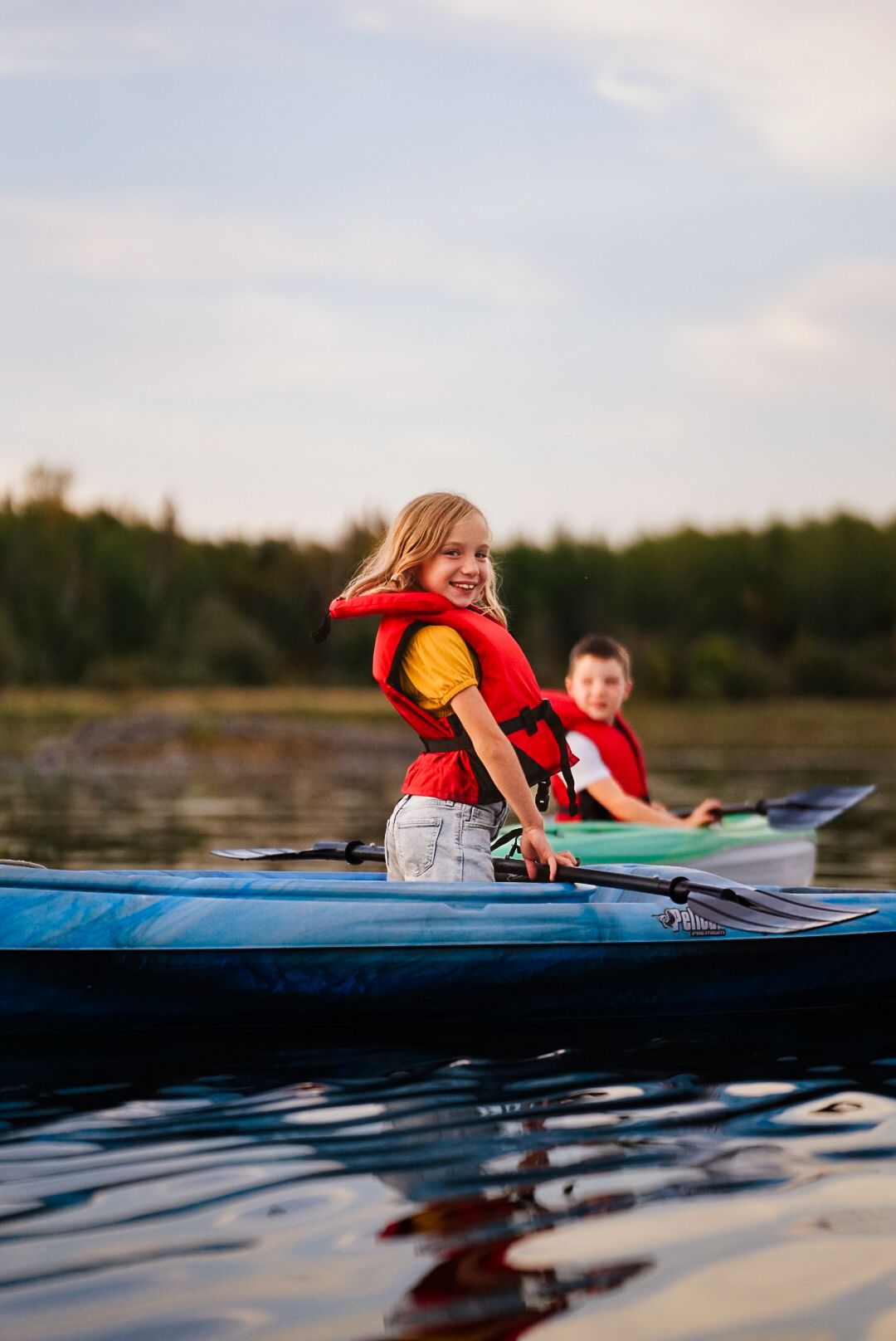 Kayakers in life vests paddle blue kayaks across calm lake waters.