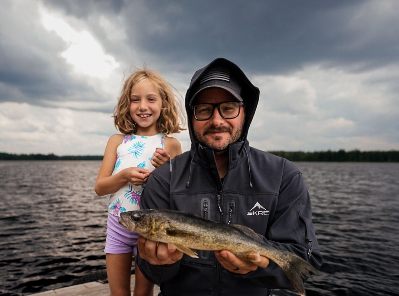 A large bass fish is displayed on a boat against a dramatic cloudy sky on the lake.