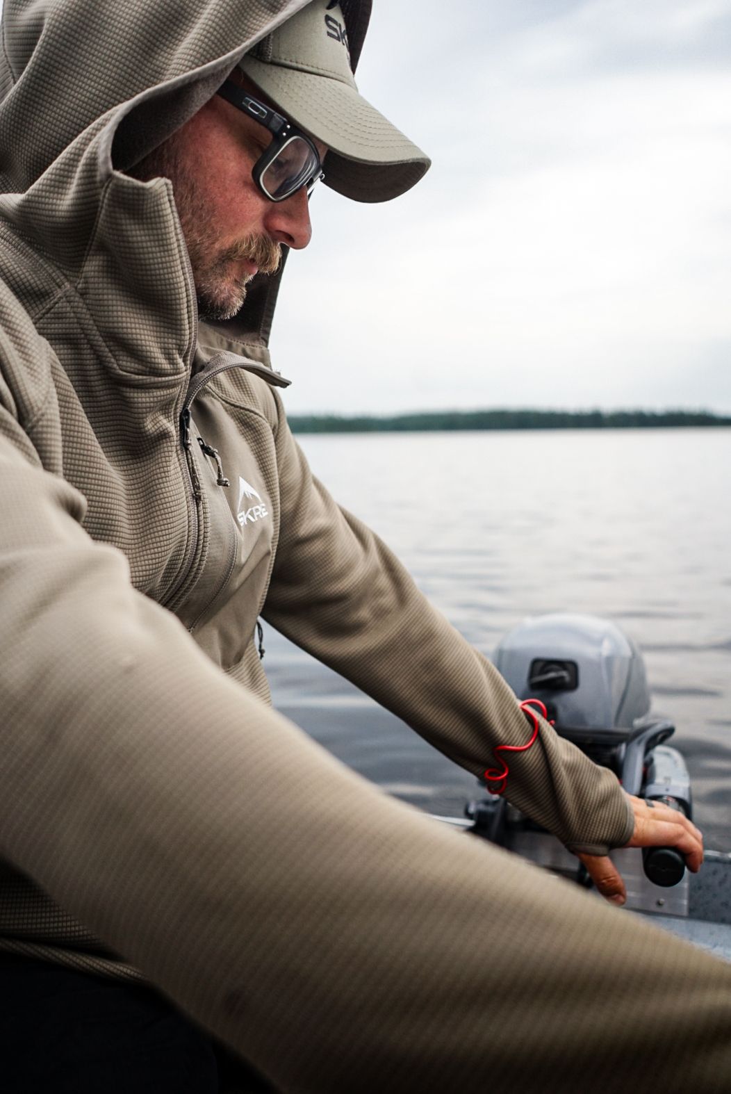Person in gray hoodie sitting in boat while fishing on cloudy day.