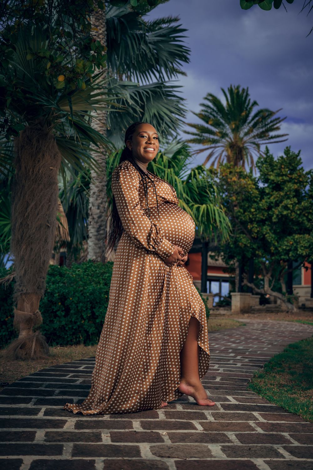 Beautiful polka dot maternity dress photoshoot in a tropical garden setting with palm trees and stone pathway.