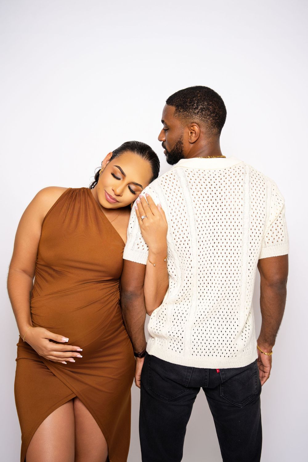 Intimate maternity portrait of couple in casual wear against white background.