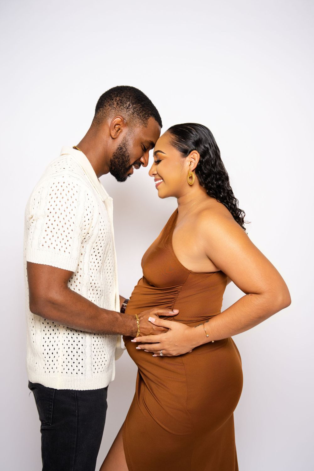 Couple shares an intimate moment in studio maternity shoot wearing brown and white.