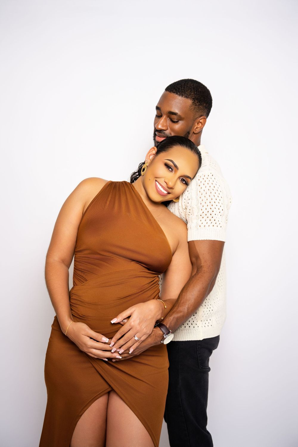 Loving couple embraces during maternity photoshoot against white background.