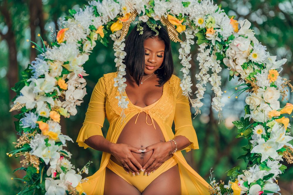Glowing maternity portrait under floral arch with white and yellow blooms.